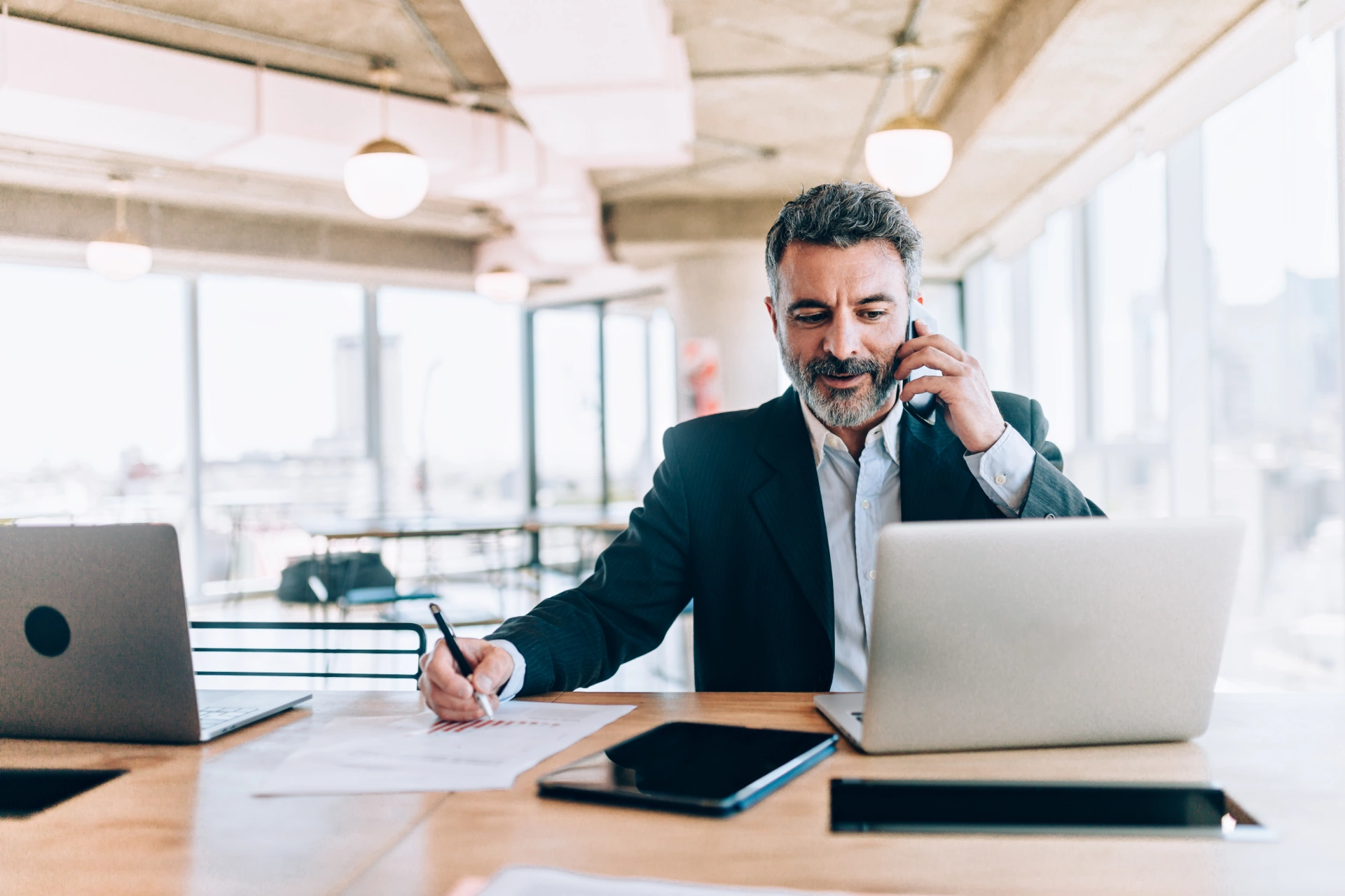 Man in a suit working on a laptop and talking on the phone in a modern office