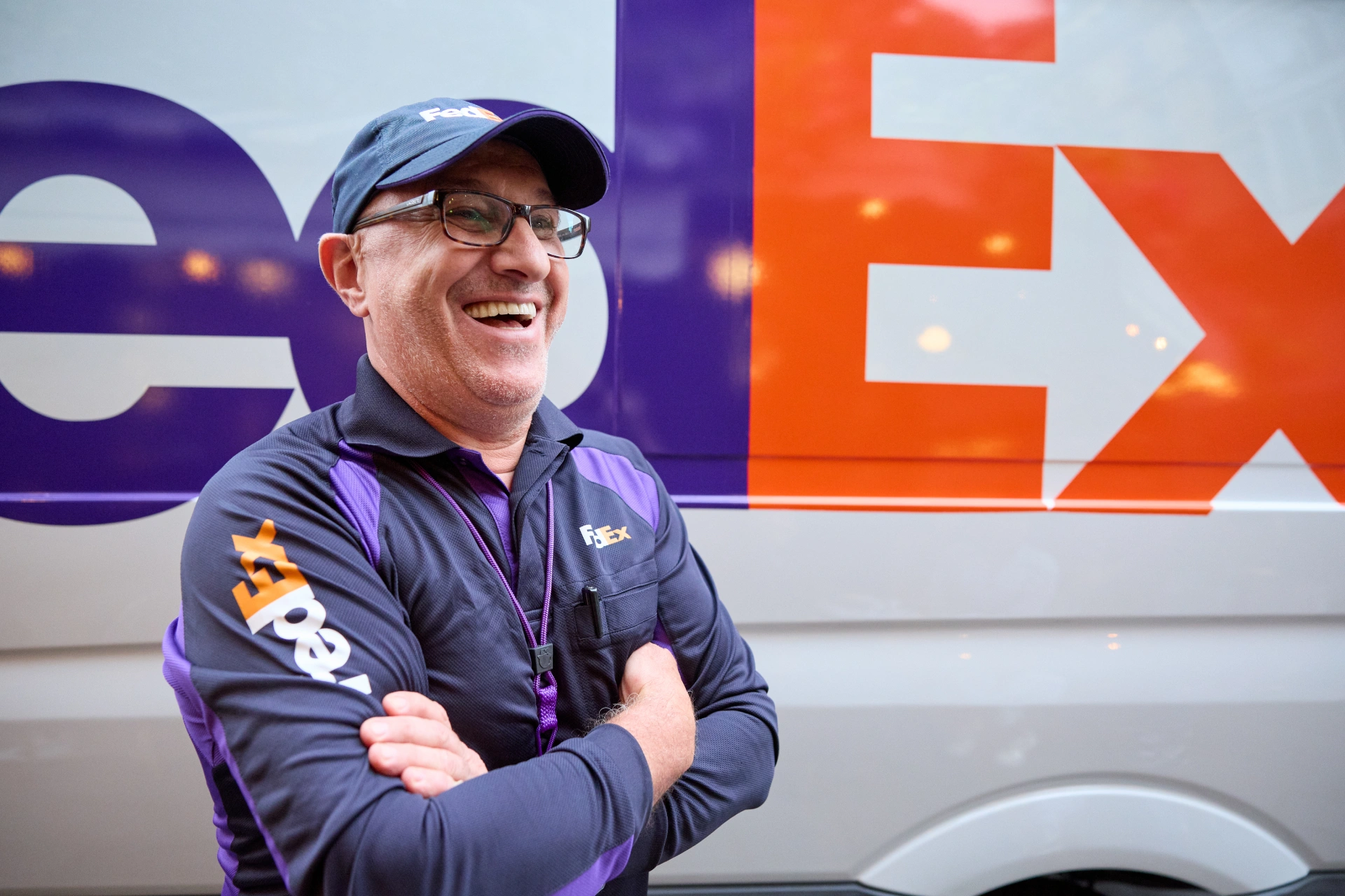 Smiling FedEx worker in uniform stands in front of a FedEx van